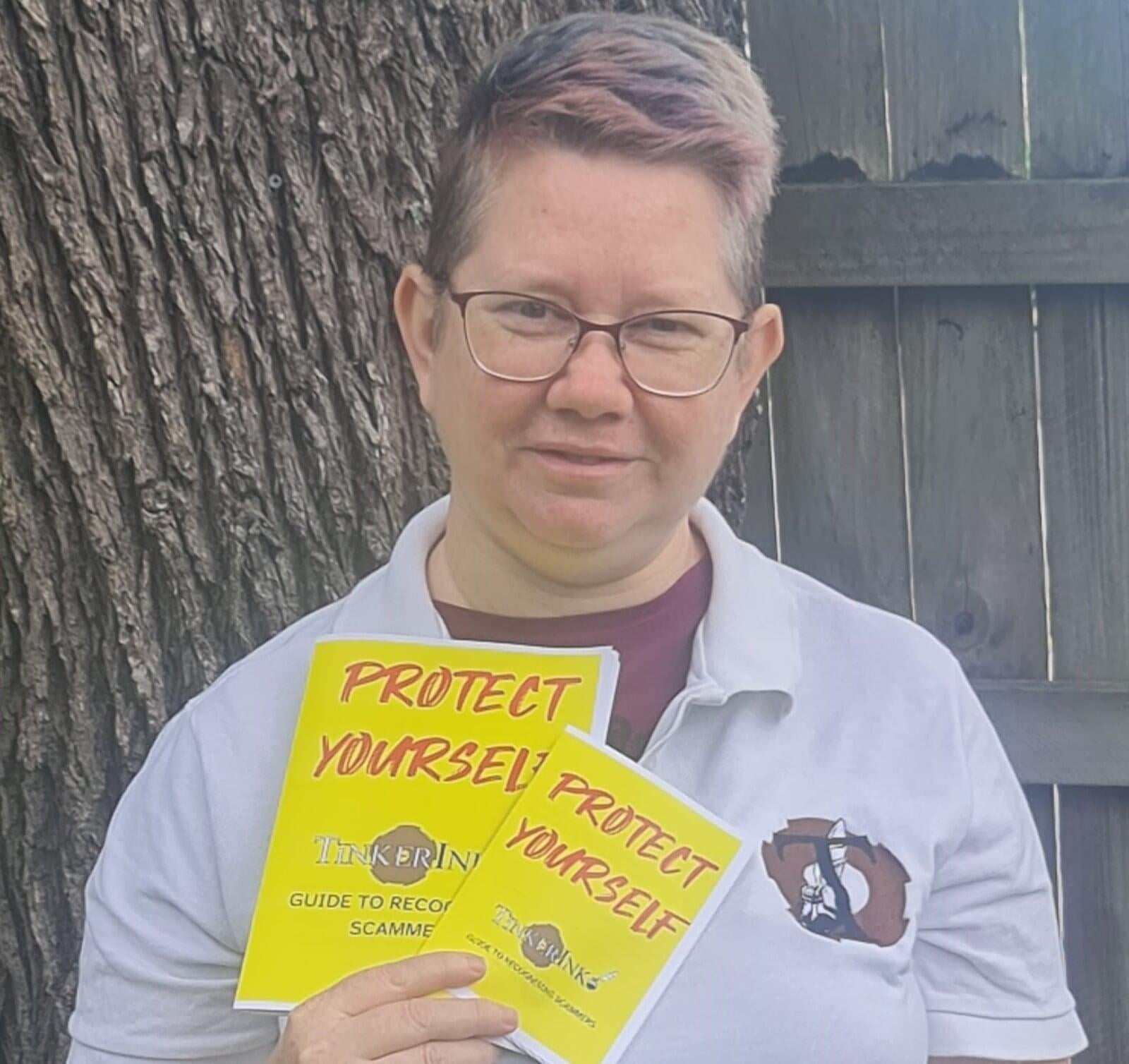 Image of Kristine Sihto, Documentation Specialist at TinkerInk and author of Protect Yourself: TinkerInk Guide to Recognising Scammers, holding our new guide in both regular and large-text versions.