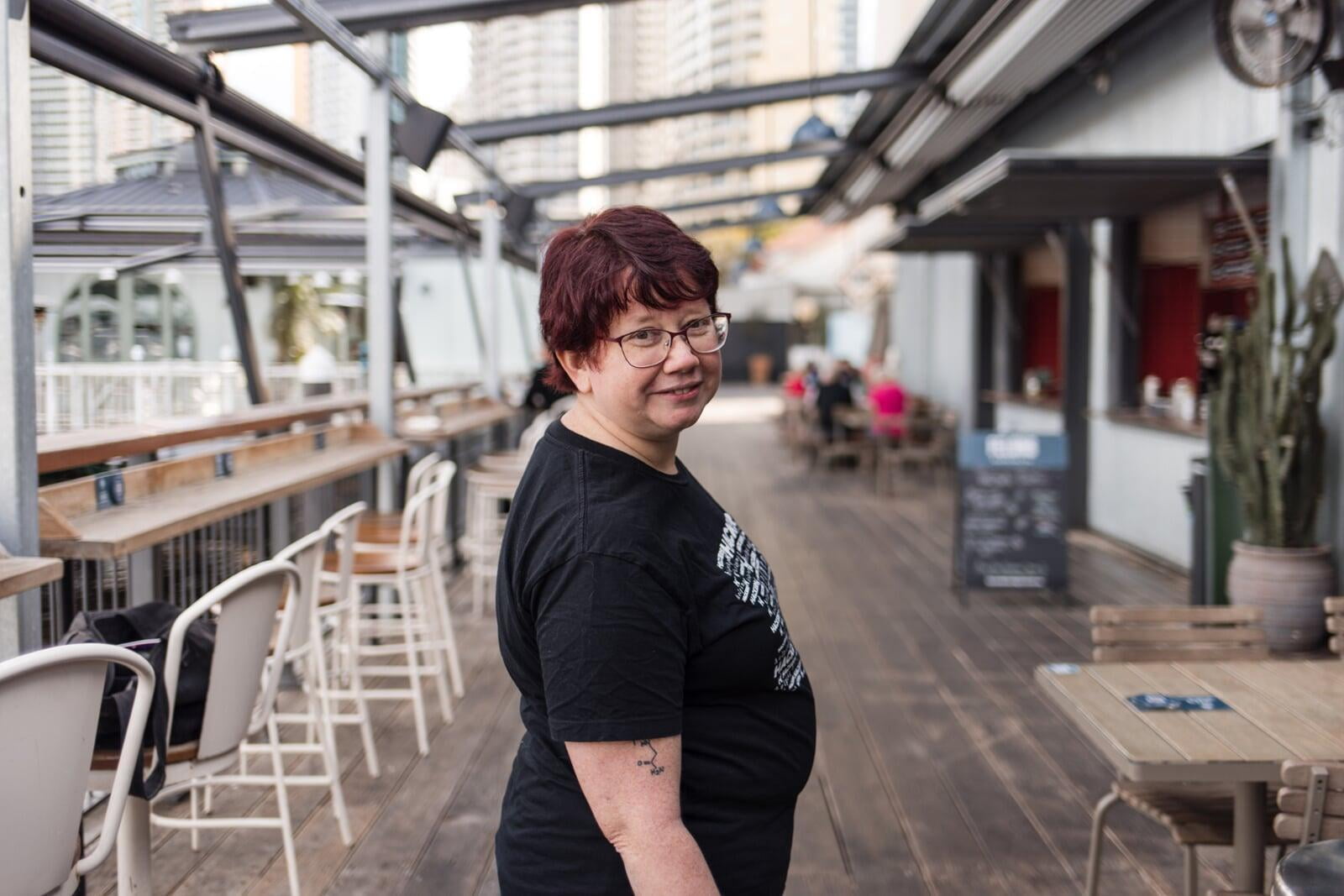 Kristine Sihto smiling and looking over their shoulder at the camera. They are standing in an outdoor city location.