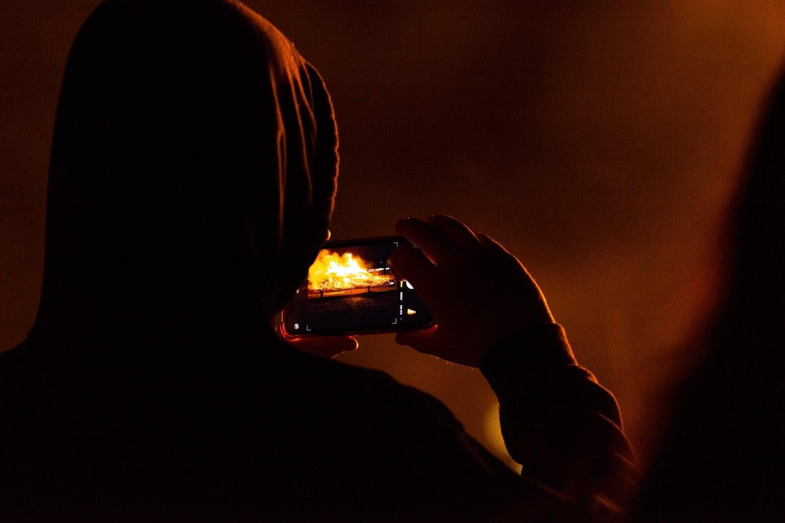 A decorative image showing a person in a hoodie looking at a phone that is displaying a large fire.